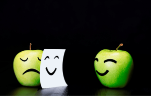 Twee groene appels. De ene appel heeft een blij gezicht, de andere appel is verdrietig, maar verbergt dit met een stuk papier waarop een blij gezicht staat. Een vorm van liegen