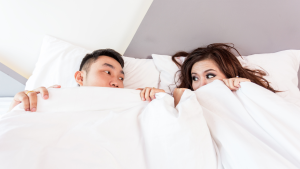 Man en vrouw liggen in bed met de dekens over zich heen getrokken en kijken elkaar vragend aan