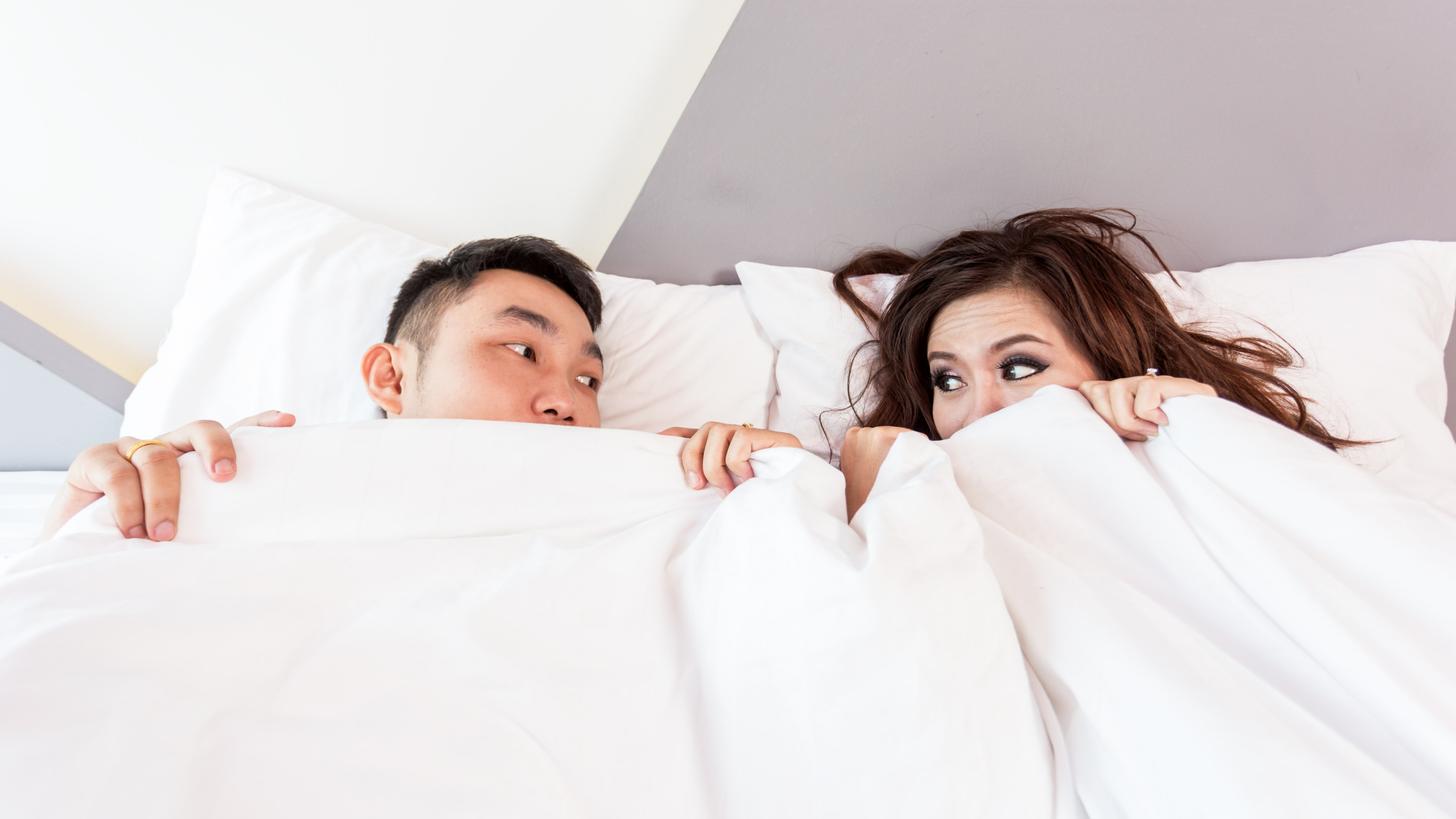 Man en vrouw liggen in bed met de dekens over zich heen getrokken en kijken elkaar vragend aan